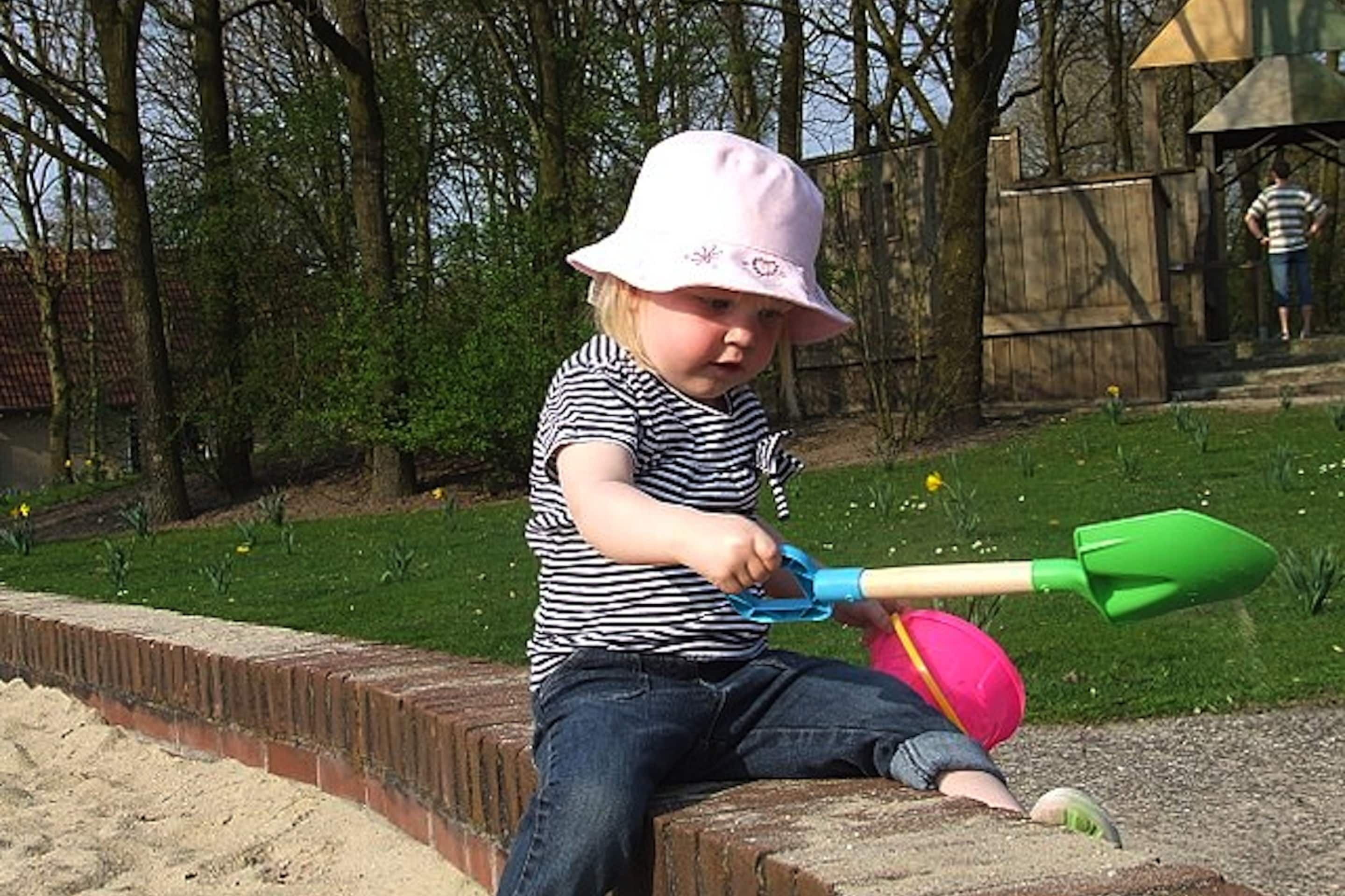 A child playing with a shovel and a ball on a brick ledge.