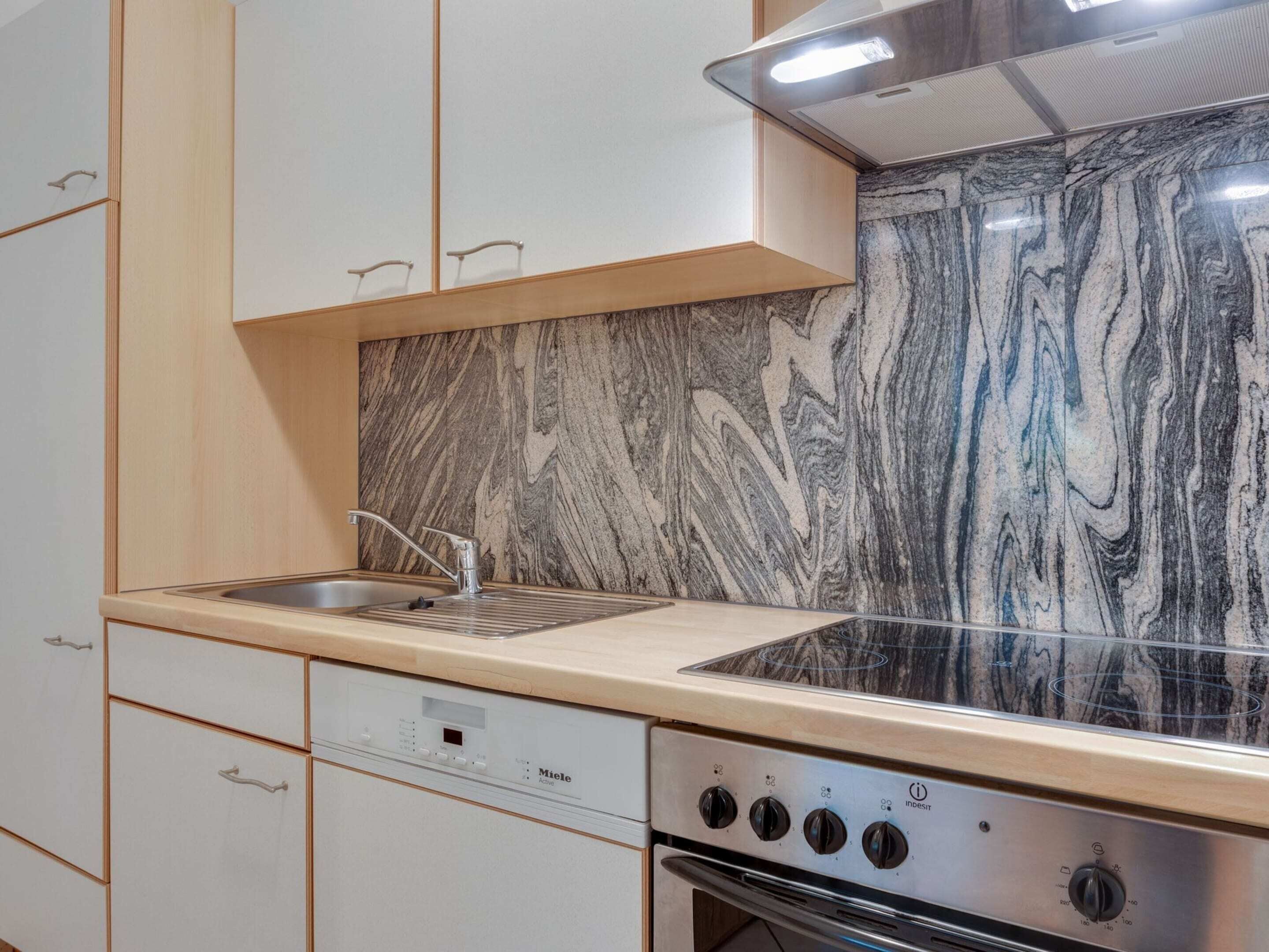 A kitchen with a marble backsplash, a stainless steel sink, and a built-in oven.