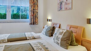Een slaapkamer met een bed, twee nachtkastjes, een raam met gordijnen en een schilderij aan de muur.