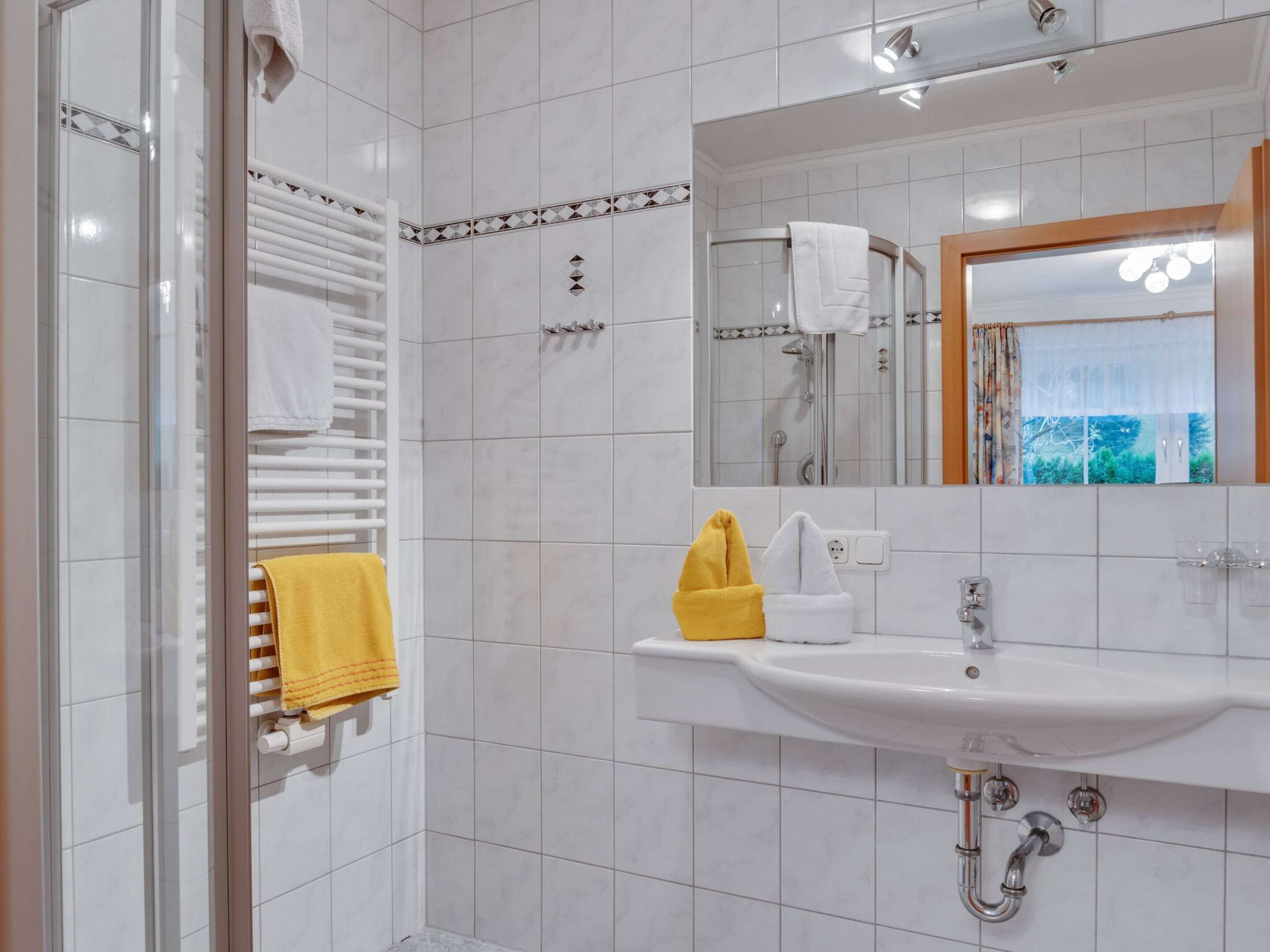 A modern bathroom with a glass shower enclosure, a white sink with a mirror above it, and a towel rack with a yellow towel.
