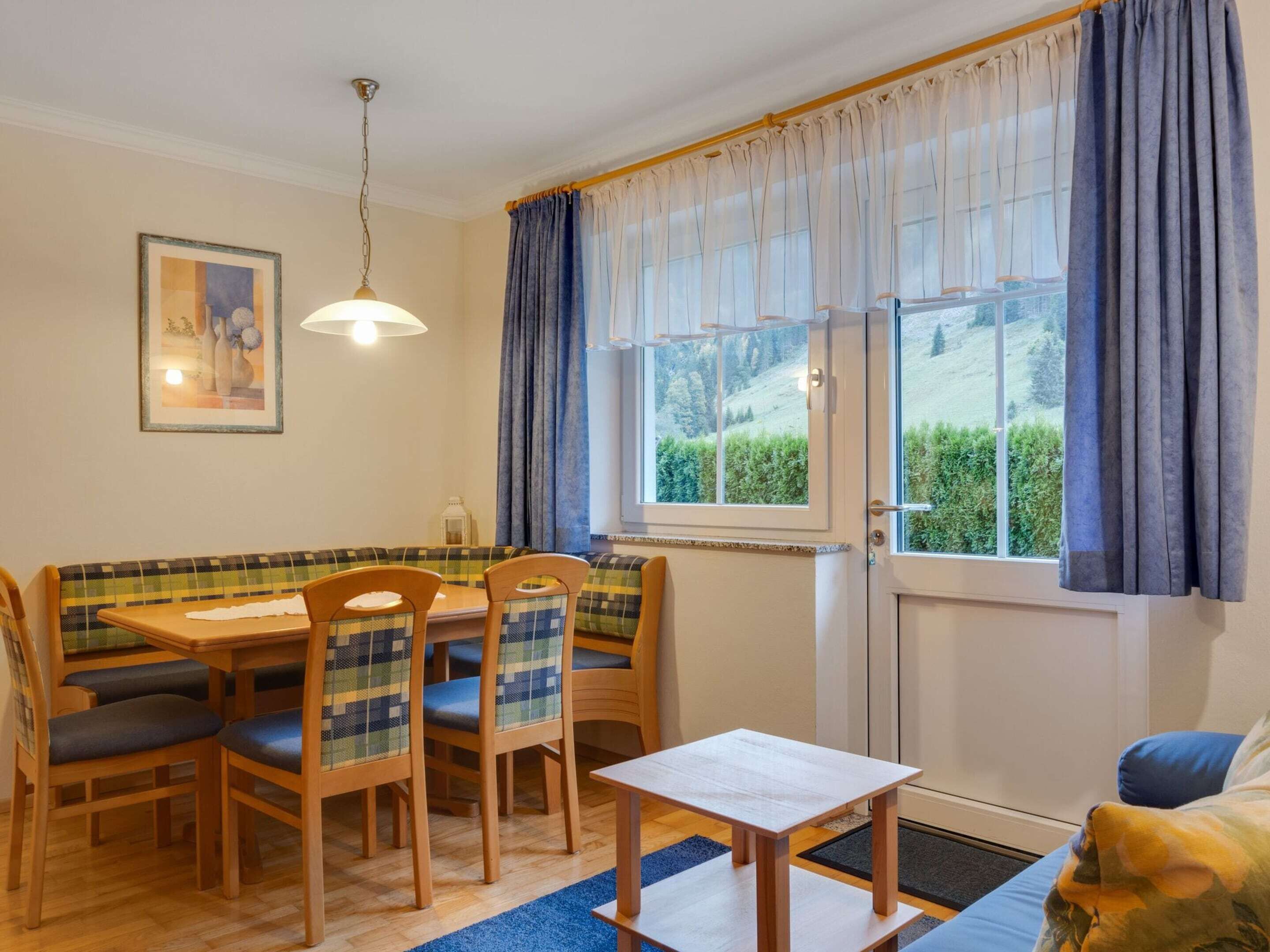 A dining area with a wooden table and chairs, a bench, and a view of greenery outside.