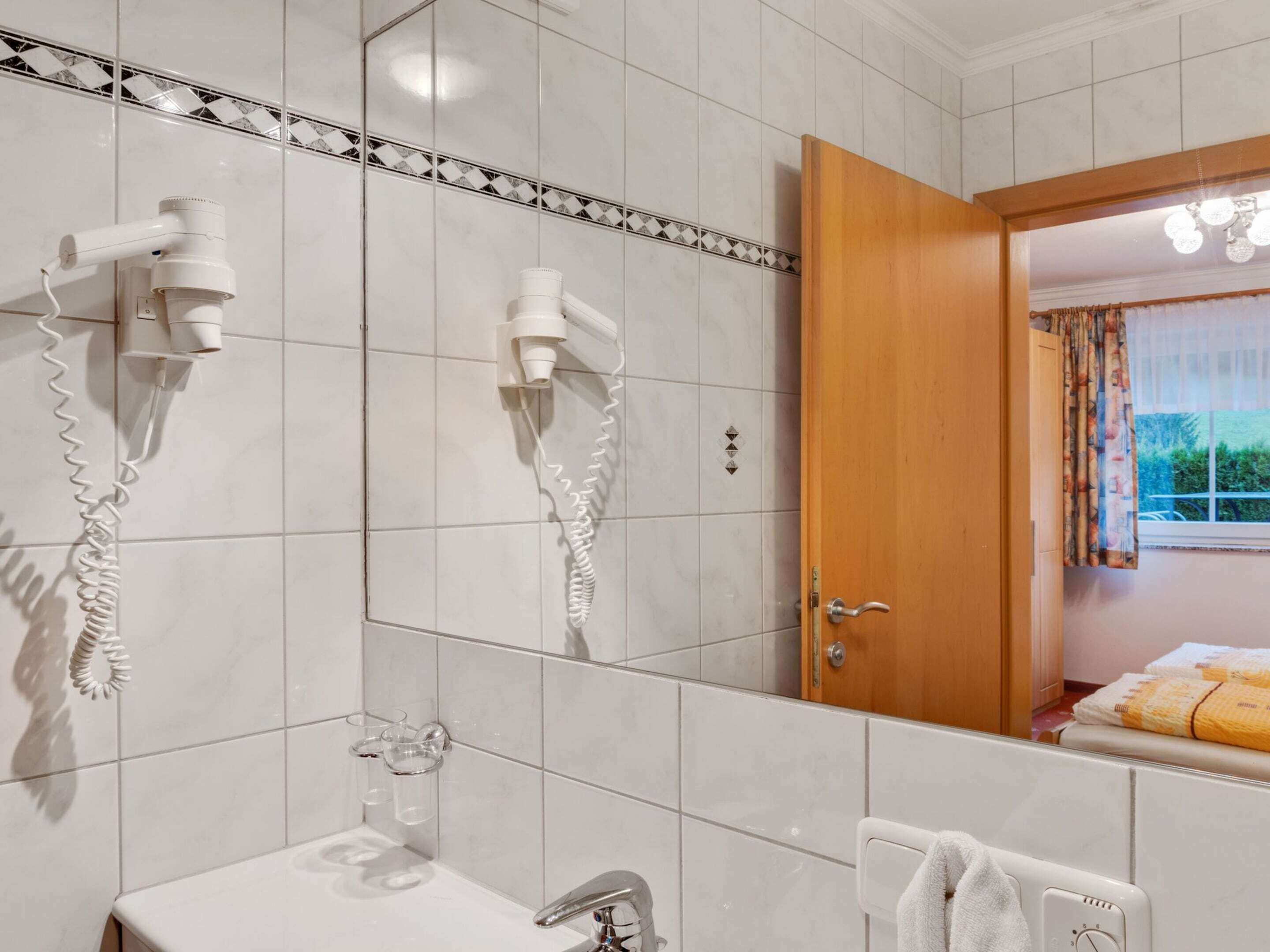 Une salle de bain équipée de deux sèche-cheveux fixés au mur, d’un lavabo avec un robinet et d’un miroir.