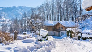 Una baita di legno con tetto imbiancato dalla neve, circondata da alberi innevati e con una montagna sullo sfondo.