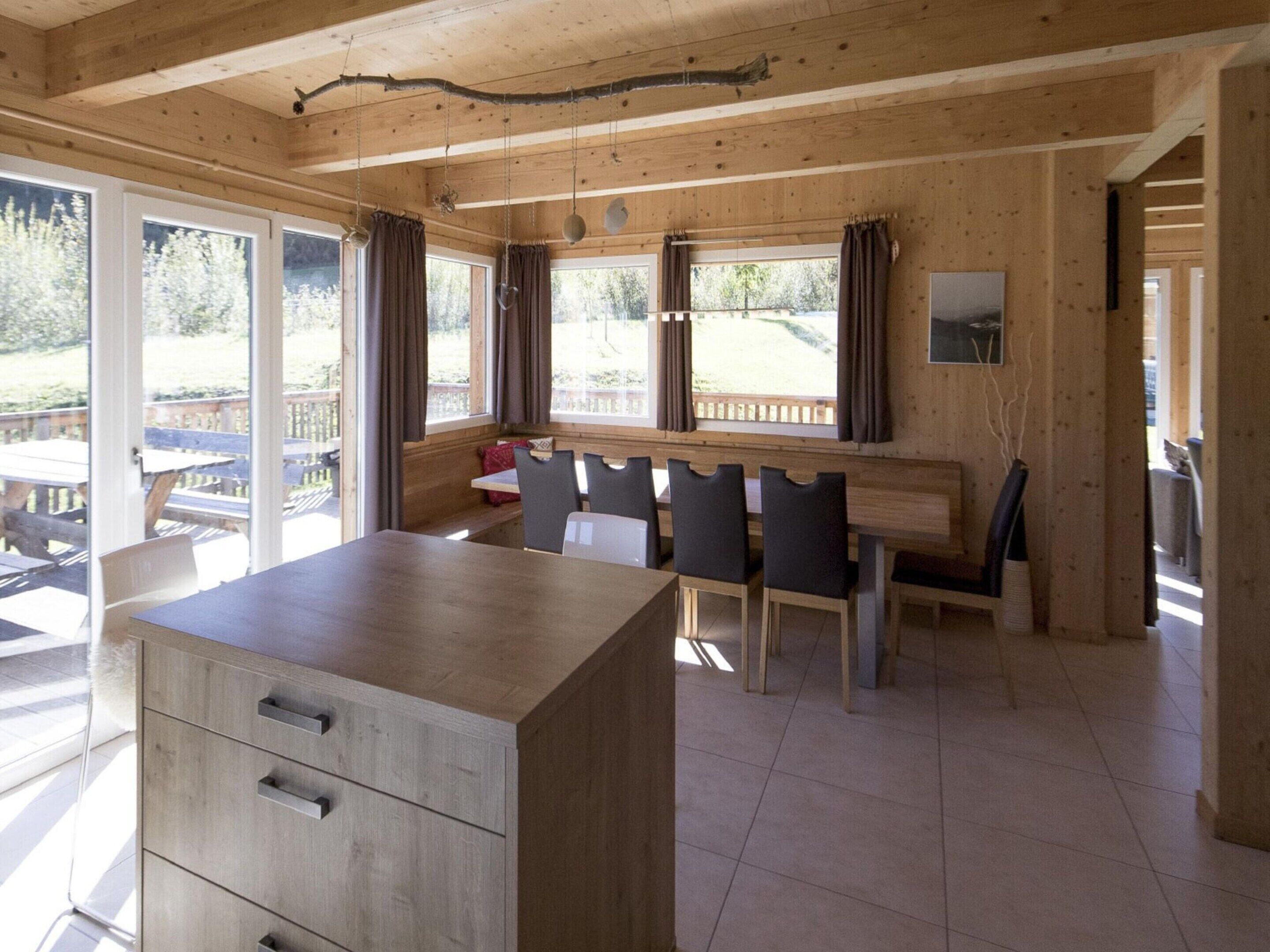 A wooden interior with a dining area, large windows, and a view of the outdoors.