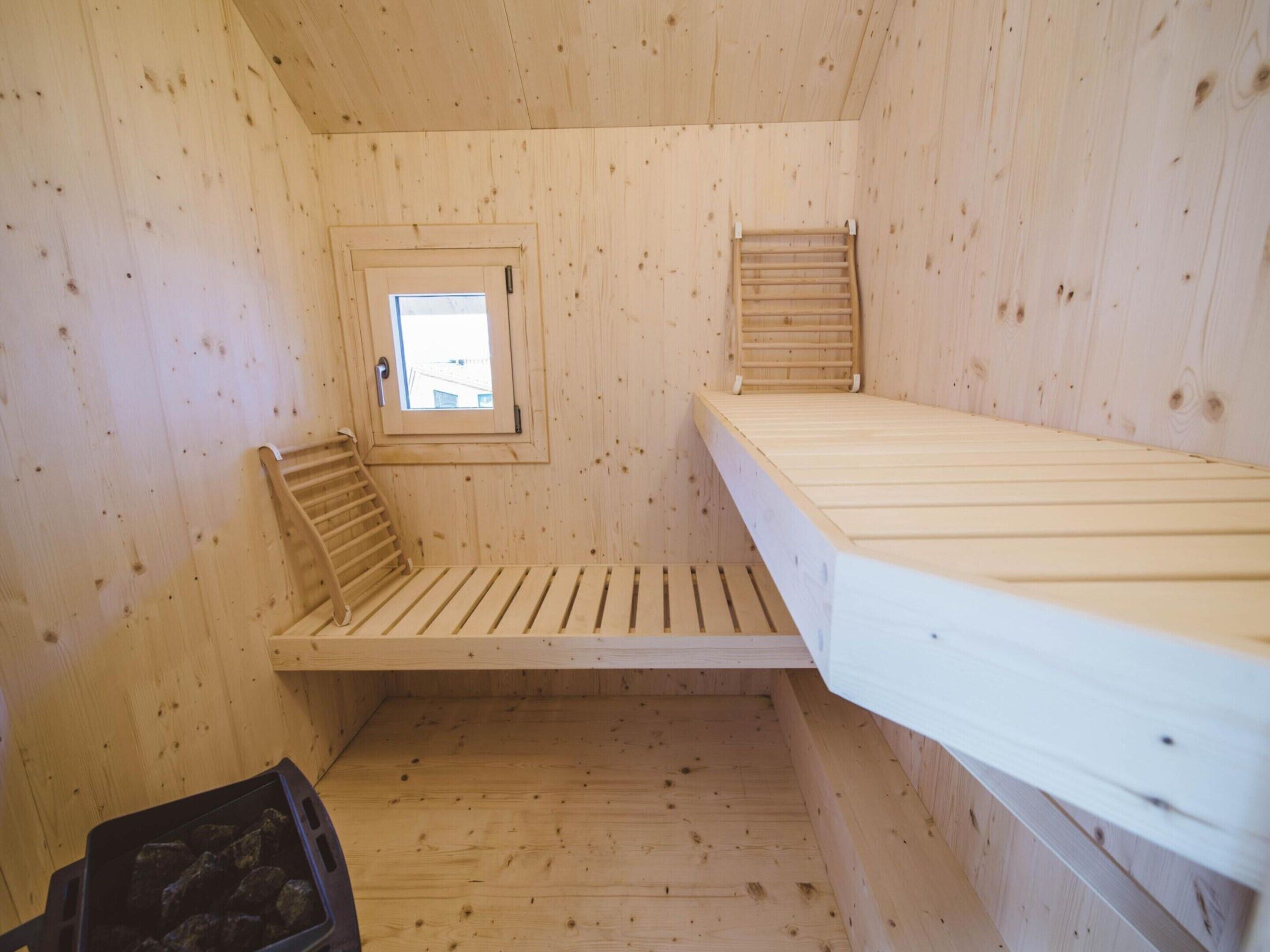 A wooden cabin room with a bunk bed, a small window, and a ladder.