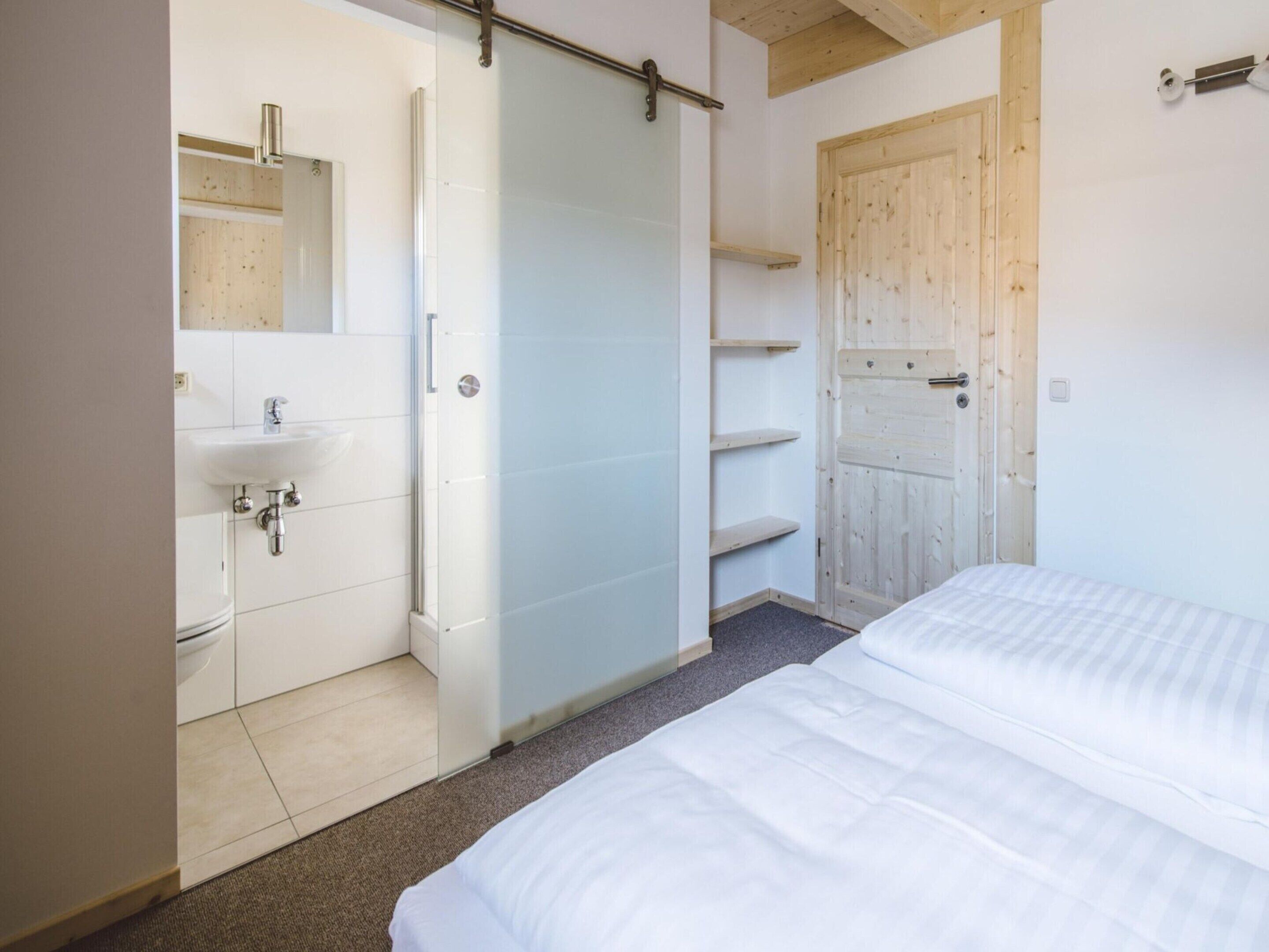 A bedroom with a bed, a bathroom with a sink, and a wooden door.