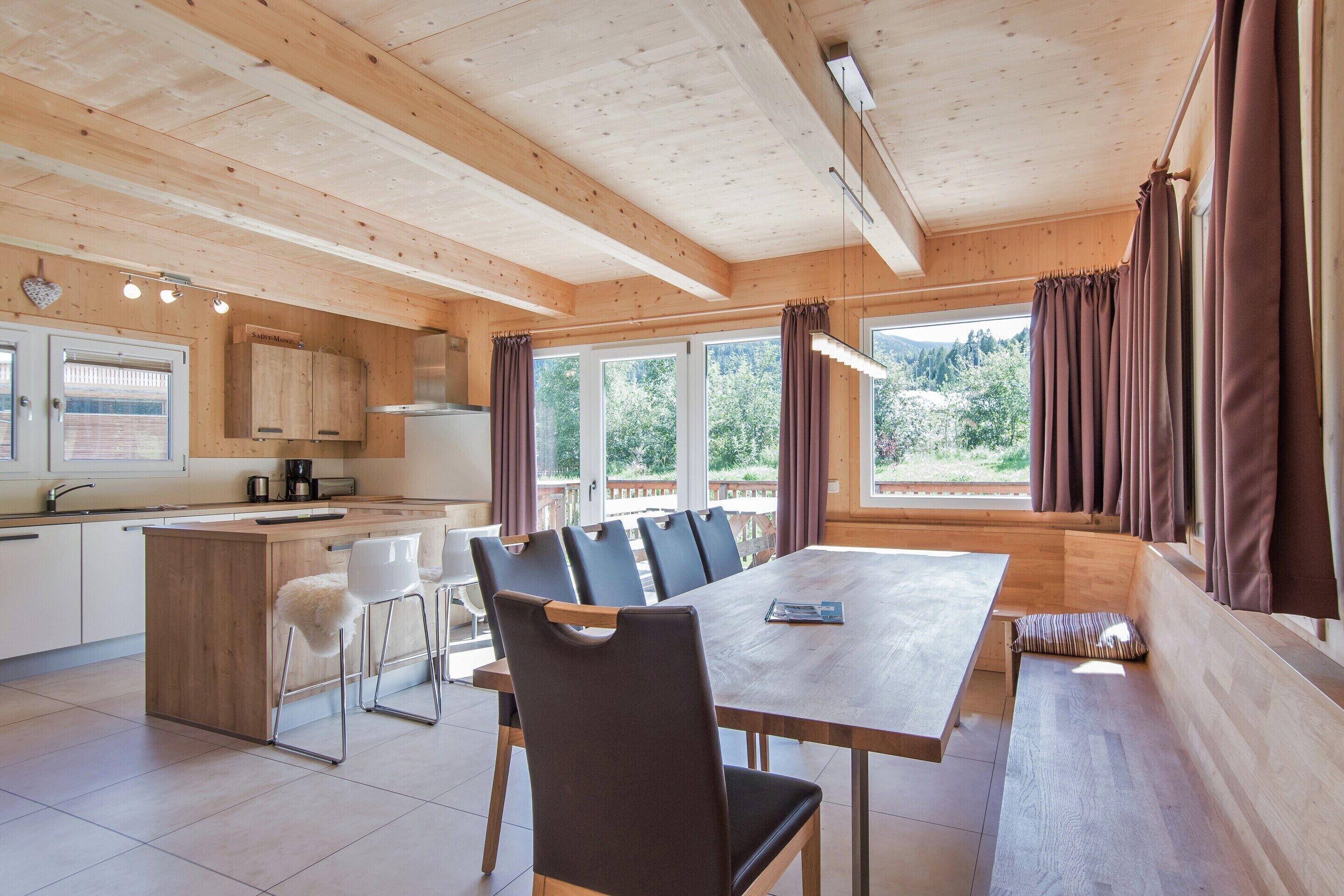 A modern kitchen with wooden cabinets, a dining area with a large table and chairs, and large windows with curtains.