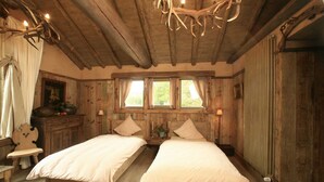 Ein rustikales Schlafzimmer mit zwei Betten, Holzböden, einer Chandelüster und einem Fenster mit Vorhängen.