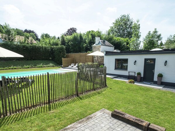 A pool with lounge chairs, a wooden fence, and a white building with a black door.