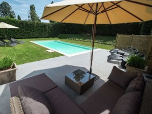 A backyard with a swimming pool, outdoor furniture, and a pergola with an umbrella.