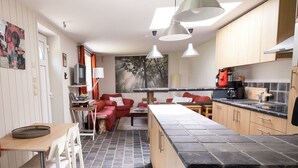 A modern kitchen with a central island, wooden cabinets, and a dining area with red chairs.