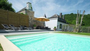 A rectangular swimming pool with clear blue water, surrounded by a stone wall and a wooden fence.