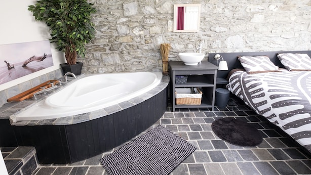 A bathroom with a stone wall, a bathtub, a sink, a mirror, and a potted plant.