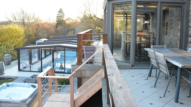 Une terrasse extérieure moderne dotée d’un jacuzzi, d’une terrasse en bois et d’un espace repas clos par des baies vitrées.