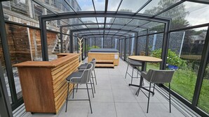 Une terrasse extérieure couverte, dotée d’un bar en bois, de sièges et d’un jacuzzi.
