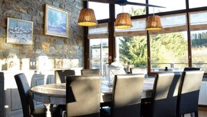 Un espace repas avec des murs en pierre, de grandes fenêtres et des suspensions en osier.