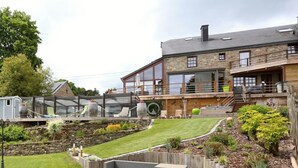Un bâtiment moderne avec une façade en pierre, un espace extérieur aménagé avec des places assises couvertes et un jardin bien entretenu.