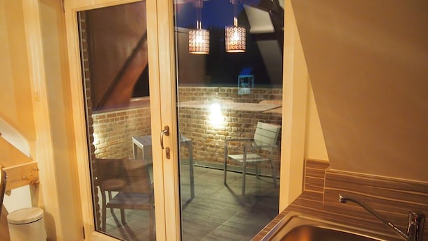 Un baño moderno con tocador de madera, lavamanos de acero inoxidable y puerta de vidrio que da a un patio exterior con pared de ladrillo, mesa y sillas.