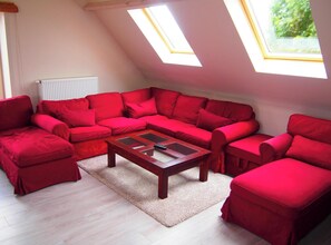 A red furnished living room with a wooden coffee table, a radiator, and skylights. - Spacious Home With Games (Ellezelles)