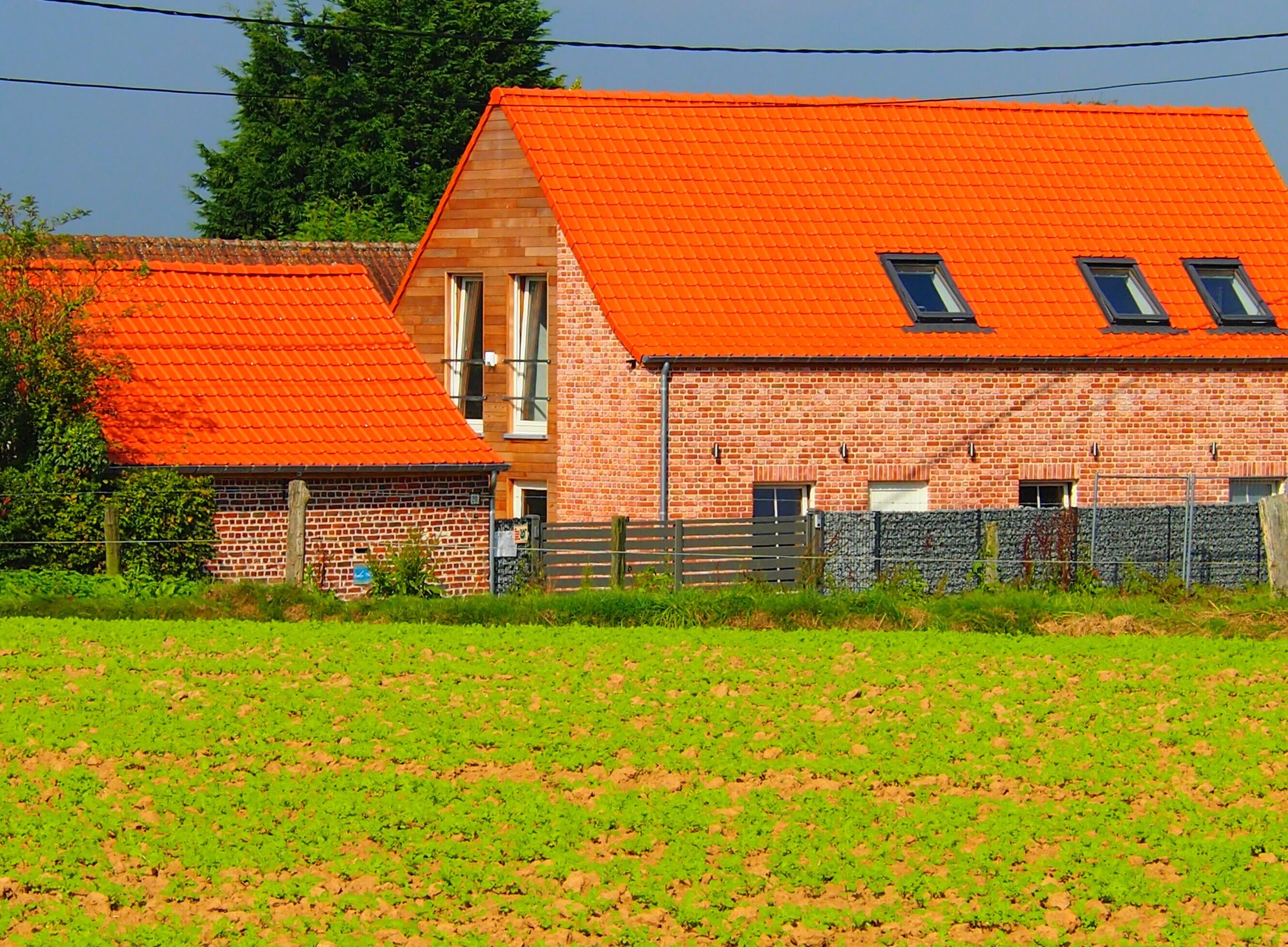 Een bakstenen schuur met een rood dak en een kleinere aanbouw.
