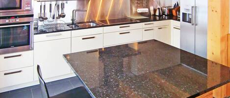 A modern kitchen with stainless steel appliances, white cabinetry, and a granite countertop.