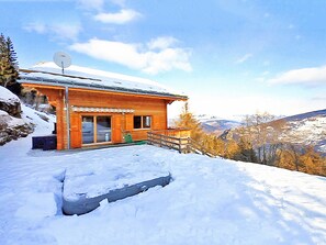 Une cabane en bois dotée d’un balcon, entourée de neige et de montagnes.