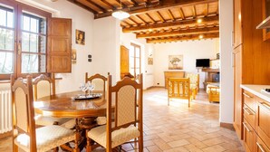 A spacious dining area with a wooden table and chairs, a kitchen with wooden cabinets, and a view through an open door. - Villa in Lisciano Niccone With Pool & Nature (Lisciano Niccone)