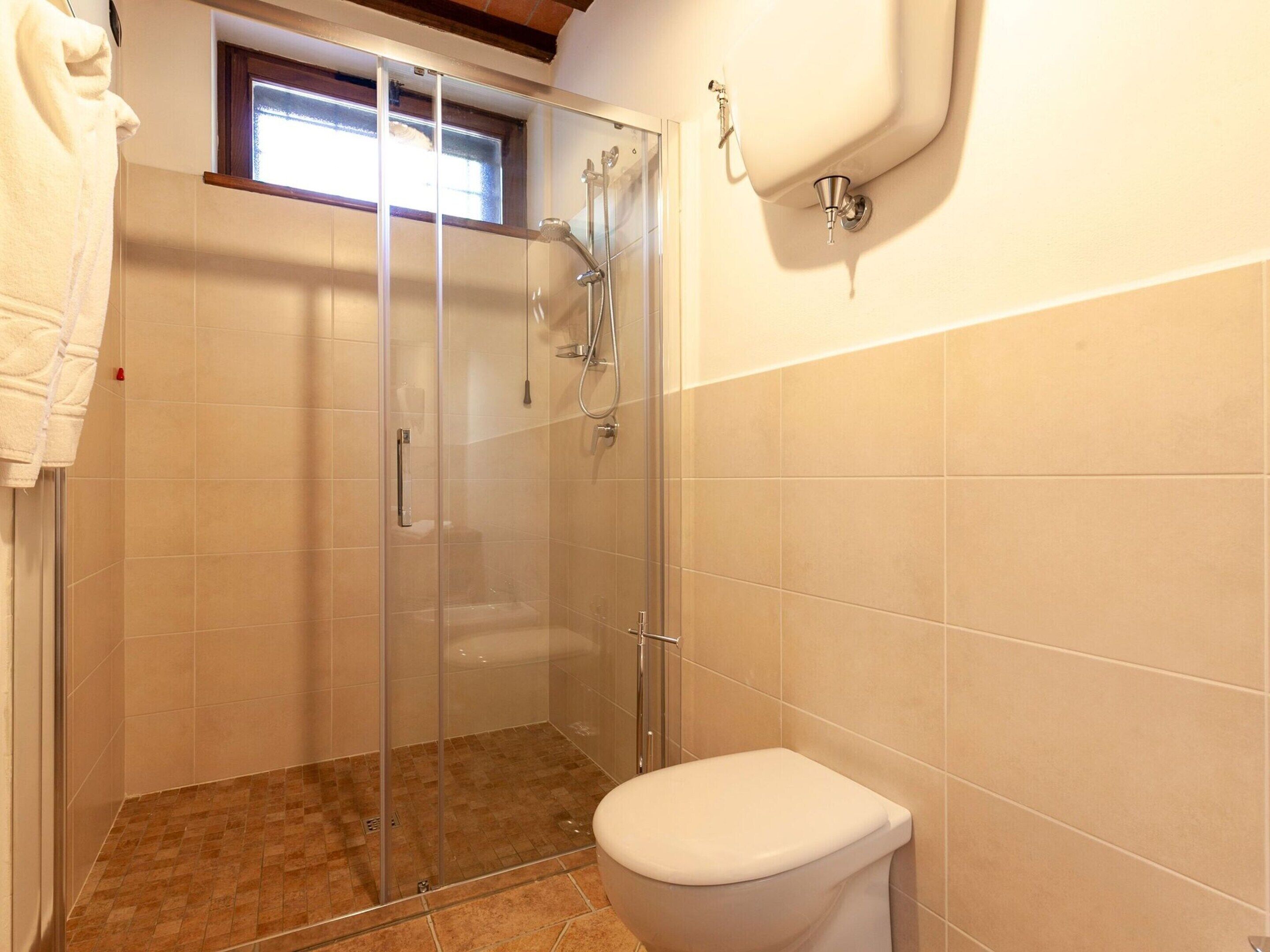 Ein Badezimmer mit Duschkabine, Toilette und einem Fenster über der Dusche.