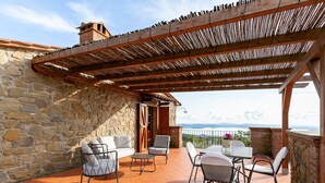 An outdoor patio with stone walls, a wooden pergola, and a table with chairs. - Villa in Lisciano Niccone With Pool & Nature (Lisciano Niccone)