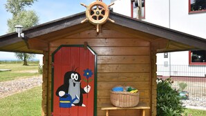 A wooden cabin with a red door, a cartoon character, and a ship's wheel. - Ferienhaus in Bastorf for 5 Personen (Bastorf)