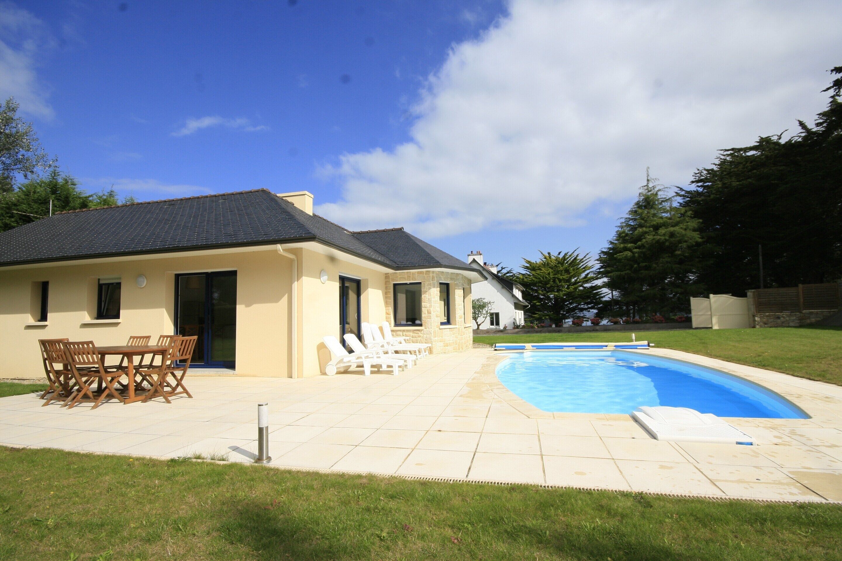 A house with a swimming pool, a patio with a table and chairs, and a lawn.