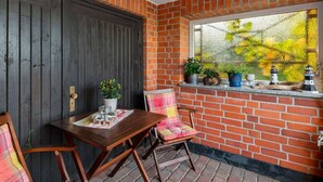 A cozy corner with a dark wooden door, a small table with a placemat, a chair, and a window with potted plants and a lighthouse model.