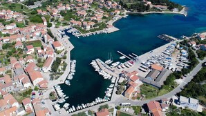 Vista aérea de un pueblo costero con un puerto deportivo, casas y un mar azul claro.