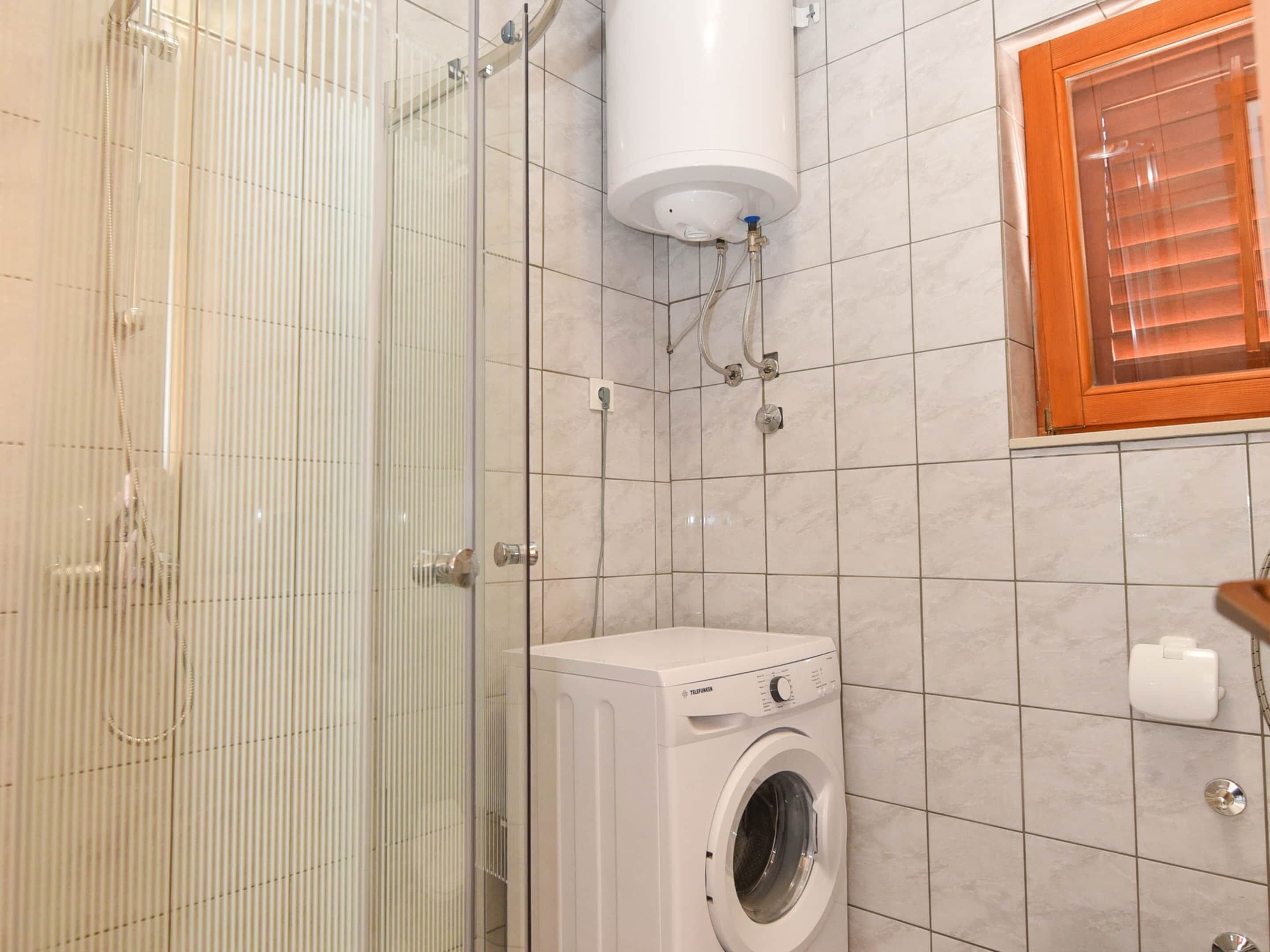 A bathroom with a glass shower enclosure, a built-in washing machine, and a toilet.
