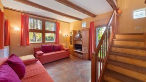 A cozy room with a wooden staircase, a sofa, a TV, and a fireplace. - Historic Half Timbered Farm in Hohnebostel near Water Sports (Langlingen)
