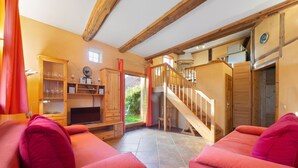 A cozy living room with red sofas, a wooden staircase, and a kitchen area visible through an open door. - Historic Half Timbered Farm in Hohnebostel near Water Sports (Langlingen)