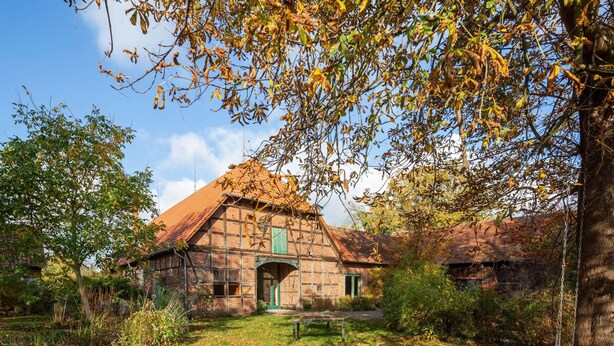 A traditional brick building with a thatched roof, surrounded by trees and a grassy area. - Historic Half Timbered Farm in Hohnebostel near Water Sports (Langlingen)