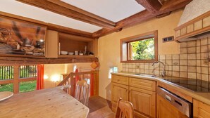 A wooden dining table with chairs, a kitchen with wooden cabinets and a tiled backsplash, and a window with a view of greenery. - Historic Half Timbered Farm in Hohnebostel near Water Sports (Langlingen)