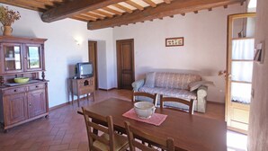 A dining area with a wooden table, chairs, a television on a stand, a sofa, and a cabinet with a vase. - Spacious Holiday Home in Montone (Montone)