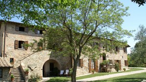 A stone building with a staircase leading to an entrance, a covered outdoor seating area, and a well-maintained lawn. - Spacious Holiday Home in Montone (Montone)