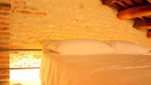 Ein Schlafzimmer mit einer Steinsäule, Holzbalkendecke und einem Bett mit weißer Bettwäsche.