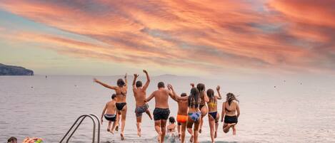 A group of people jumping off a dock into a body of water during sunset.