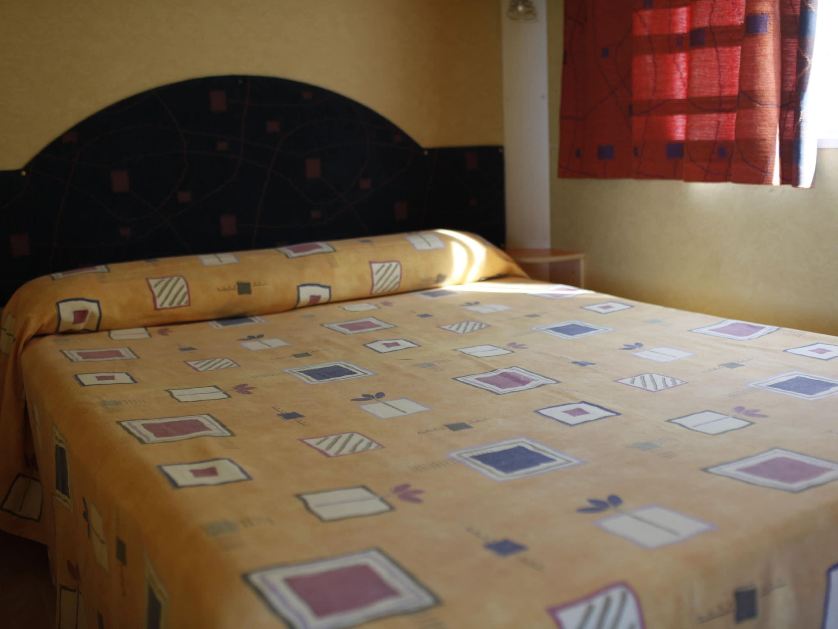 Una cama con una colcha estampada, un cabecero oscuro y una cortina roja.