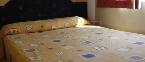 Una cama con una colcha estampada, un cabecero oscuro y una cortina roja.