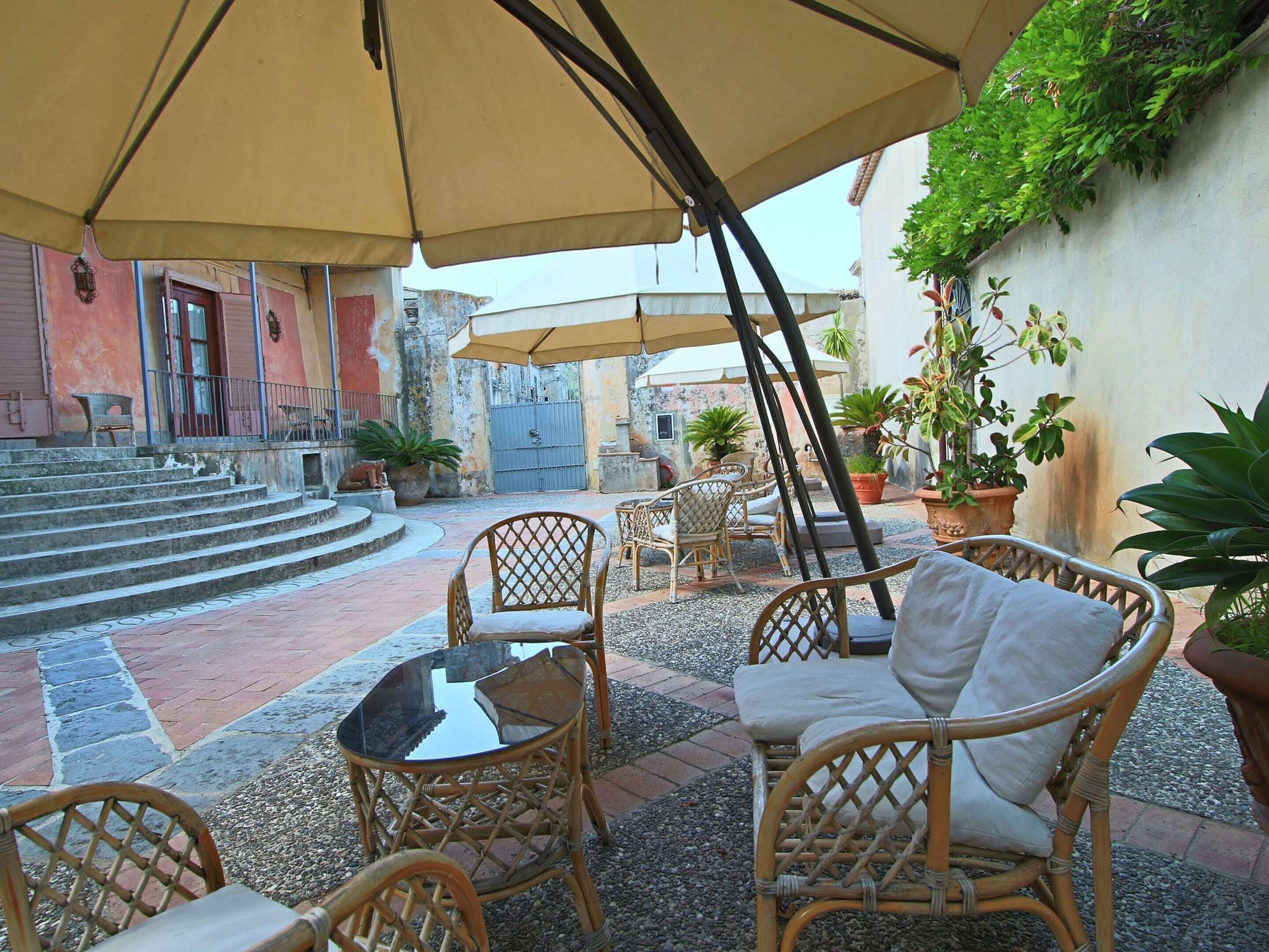 An outdoor patio area with wicker furniture, a glass table, and potted plants.