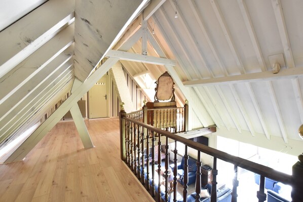 Une pièce mansardée avec des poutres en bois, un escalier et une vue sur l’espace de vie situé en contrebas.