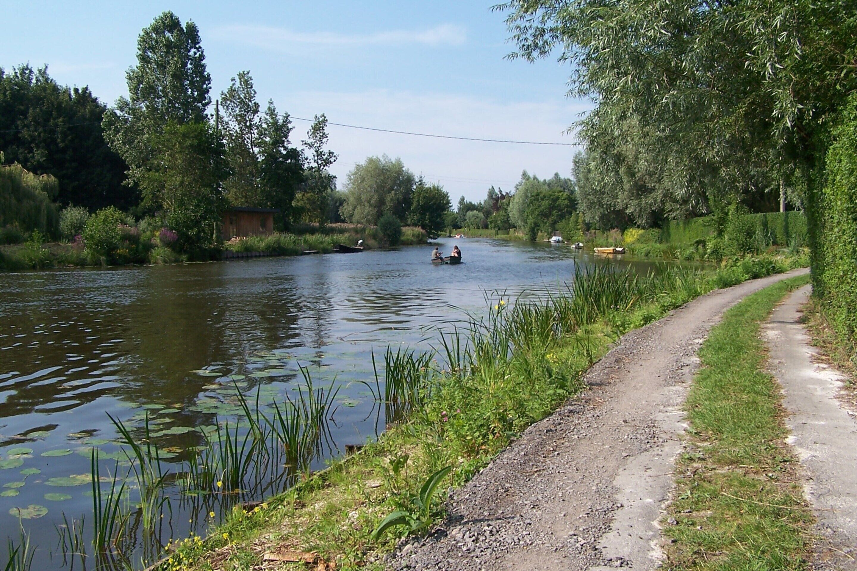Un fiume con barche, un sentiero lungo la riva e vegetazione.