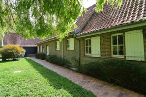 A brick building with a tiled roof, a paved pathway, and green foliage. - Holiday Home in Saint-omer Near Lake & Forest (Saint-Omer)