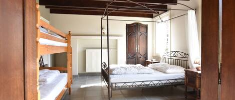 Un dormitorio con una cama con dosel, una cama individual más pequeña, un armario de madera y una mesita de noche con lámpara.