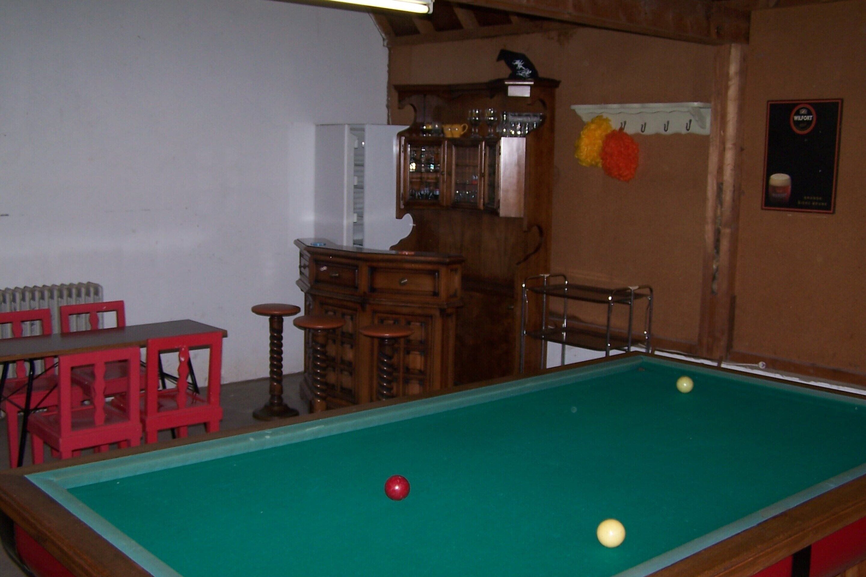 Una mesa de billar con bolas, una silla roja y un aparador de madera con puertas de cristal.